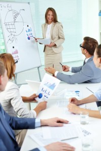 Happy top manager standing by the whiteboard and interacting with business partners at seminar